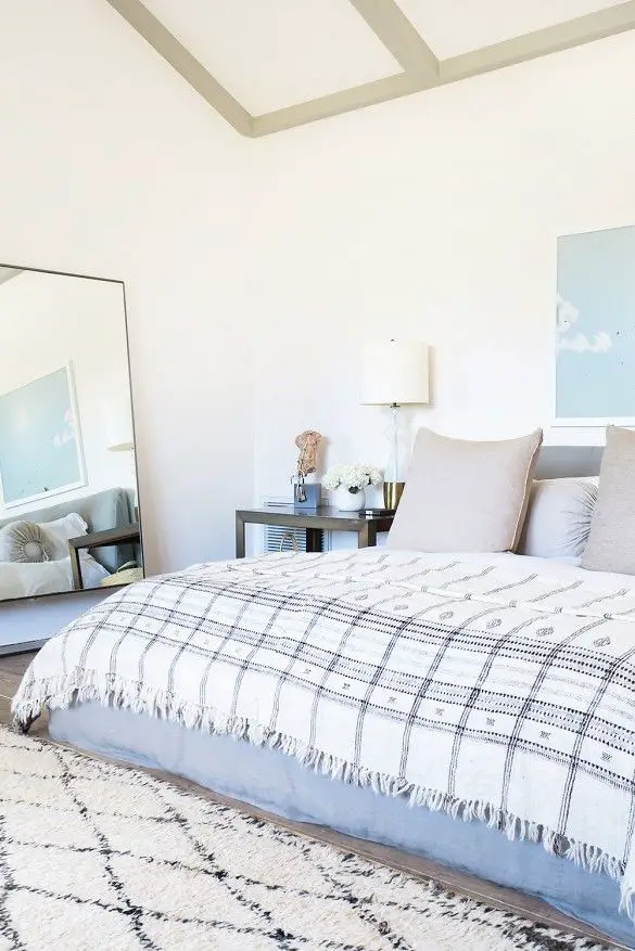 White bedroom with neutral plaid bedding, leaning mirror: 