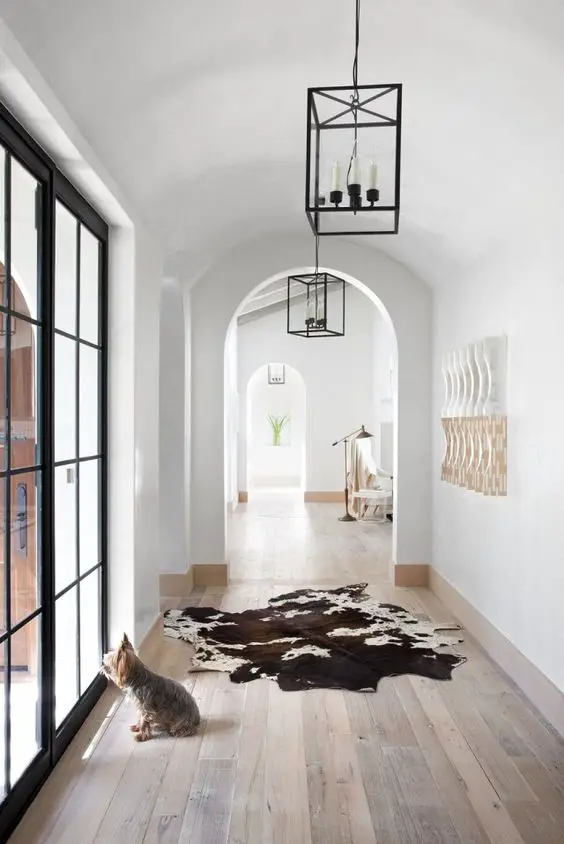 Hall with large windows, fur rug, and rustic pendant lamps. | @andwhatelse: 