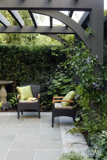 House & Home Outdoor room framed with a black painted arbour overhead, black seating and bluestone floor.