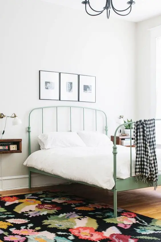 Feminine yet minimal bedroom with a floral area rug, a white sconce, and a green metal bed frame: 