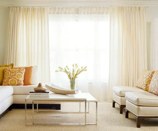creamy white walls and window treatments are the backbone of this clutter-free room. Furniture with clean lines sticks with the streamlined look. A modern nesting table pulls out for serving food and drinks. To maintain the crisp look, pick a single accent color in a modern shade, like bright orange. Replace with a new hue to change the look.