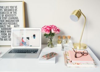 Decorated home office with flowers, picture with quote, lamp, laptop and glasses on notebooks