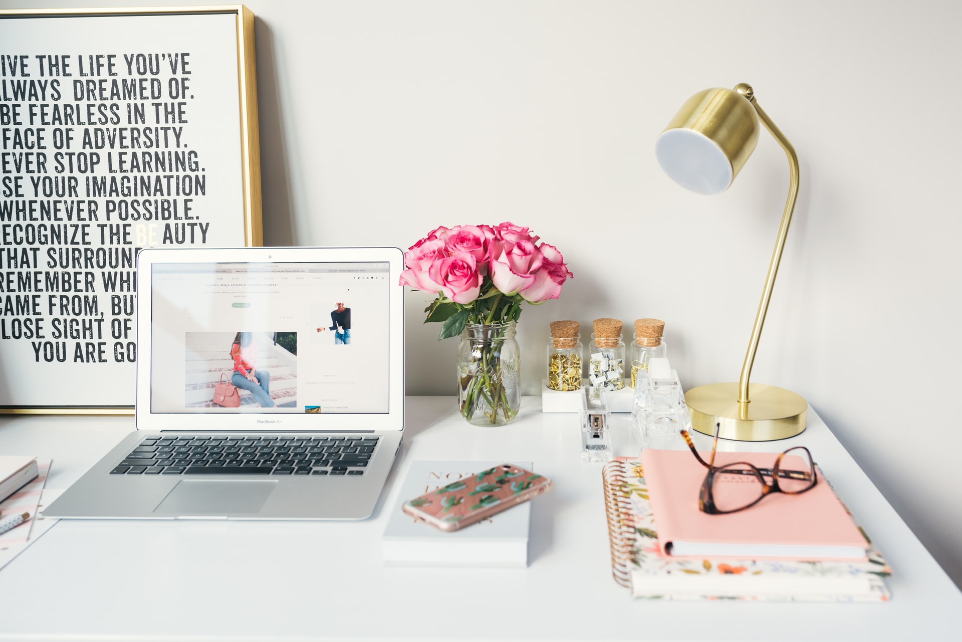 Decorated home office with flowers, picture with quote, lamp, laptop and glasses on notebooks