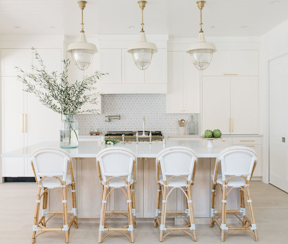 White designed kitchen with bar table and chairs, hanging lights and flowers in the vase on the table with kitchen elements in the background