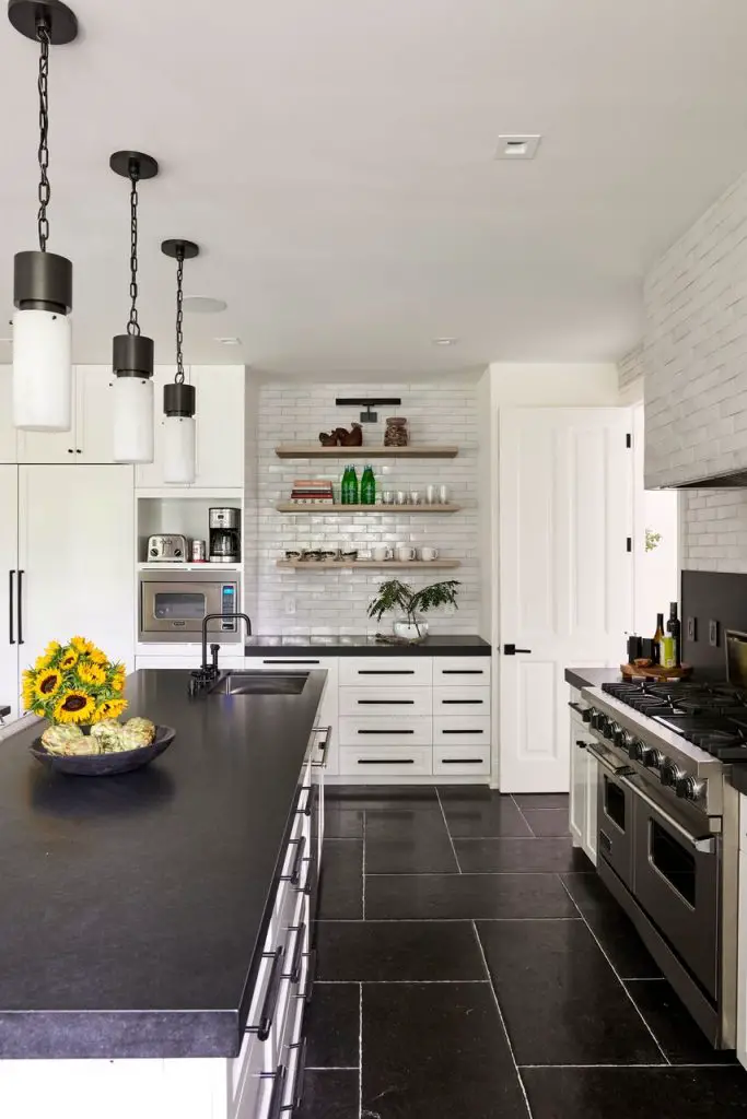 Side view of kitchen with kitchen island and kitchen elements in the background, oven and hanging lights over the island with vase and sunflowers