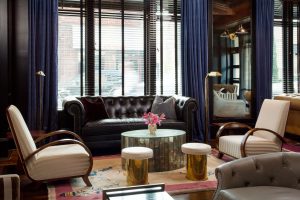 Bar in a hotel with sofa, coffee table, armchairs, chairs, carpet and window behind sofa