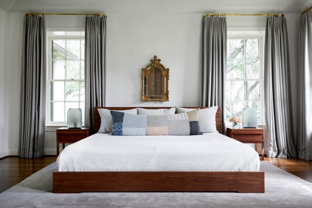 Bedroom with large double bed, wooden nightstands beside each side of the bed and behind them windows with big light gray curtains