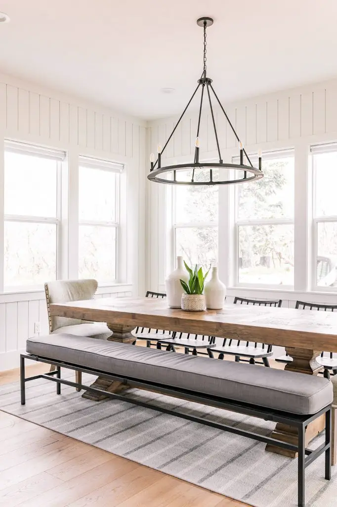 Long dining table with bench and chairs around it and wide windows in the background