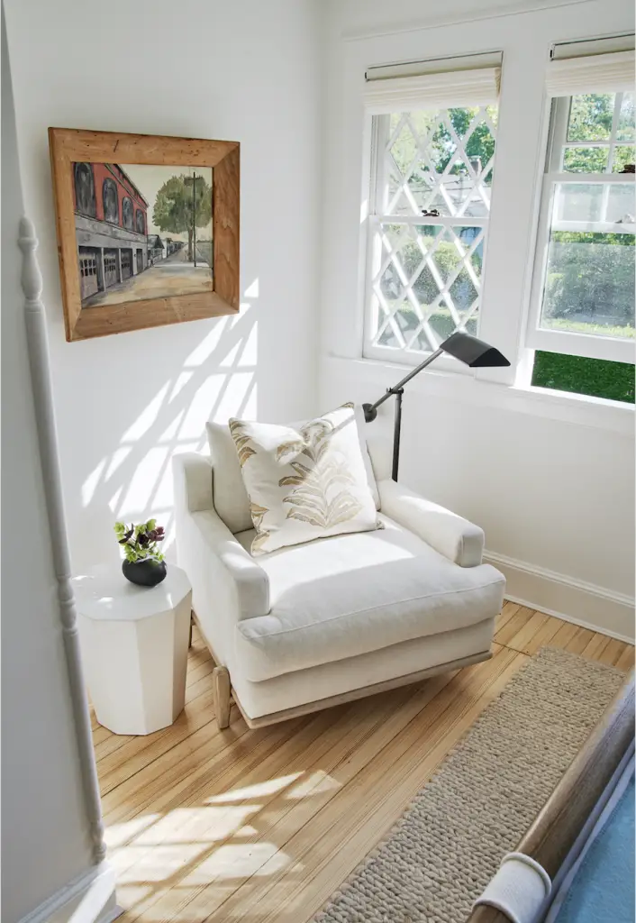Corner of the room with white  armchair, light and small coffee table with plant on it