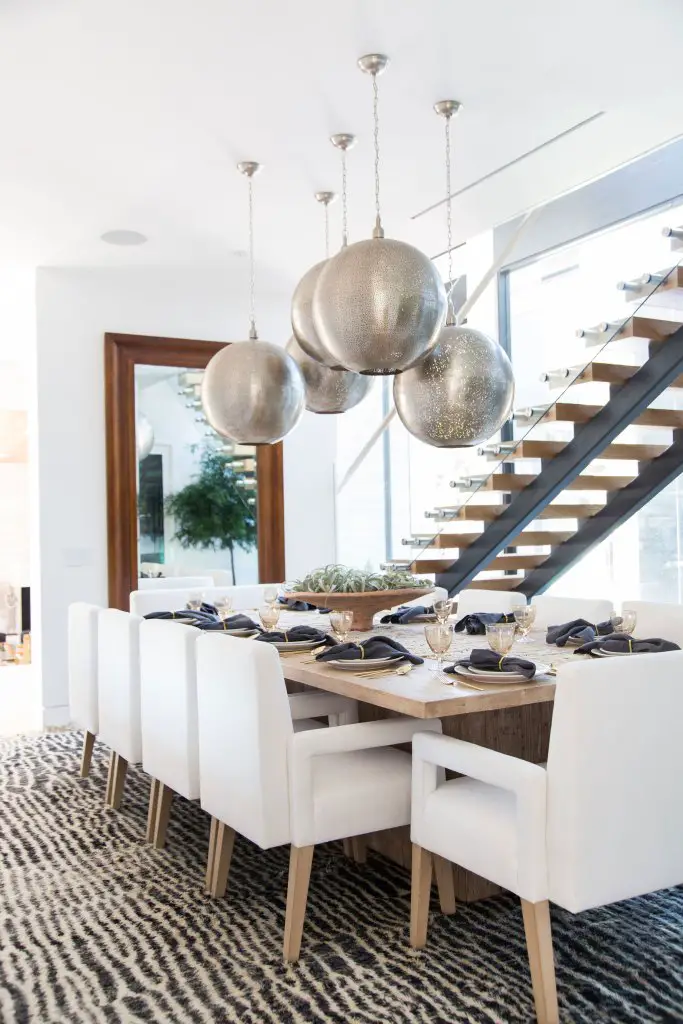 Dining space with table and white chairs around it, decorative round celling and staircase in the background