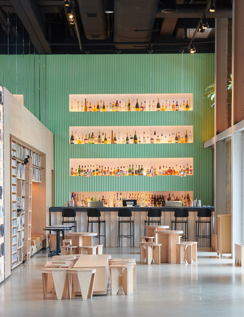 Restaurant with bar and bar chairs with beverages behind the bar and wooden chairs and tables in front of the bar