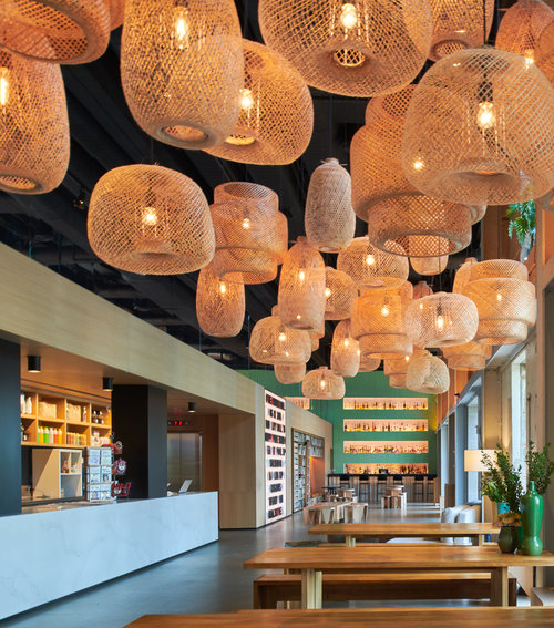 Restaurant with counter to the left, wooden tables and benches to the right and wood-woven decorative hanging lights