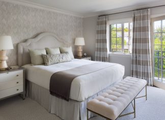 Bedroom in white and beige tones, with double bed and a bench at the bottom of the bed