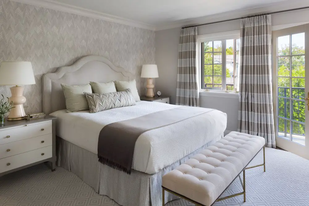 Bedroom in white and beige tones, with double bed and a bench at the bottom of the bed