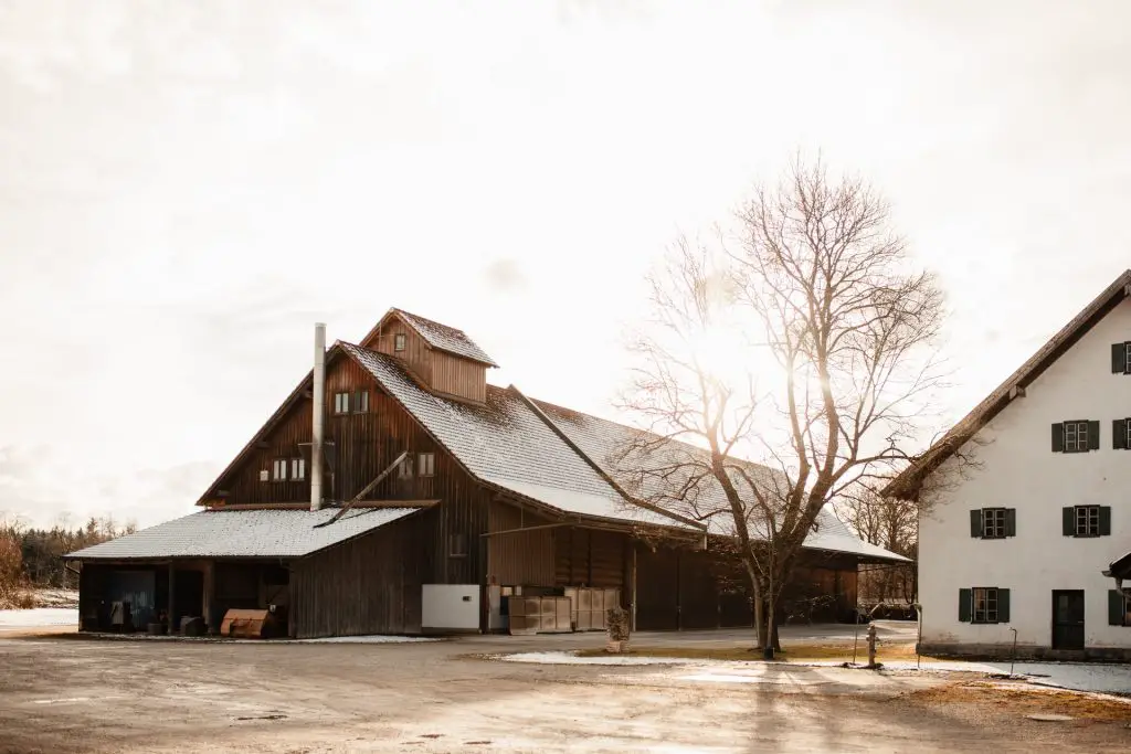 A large barn with a tree and a house beside