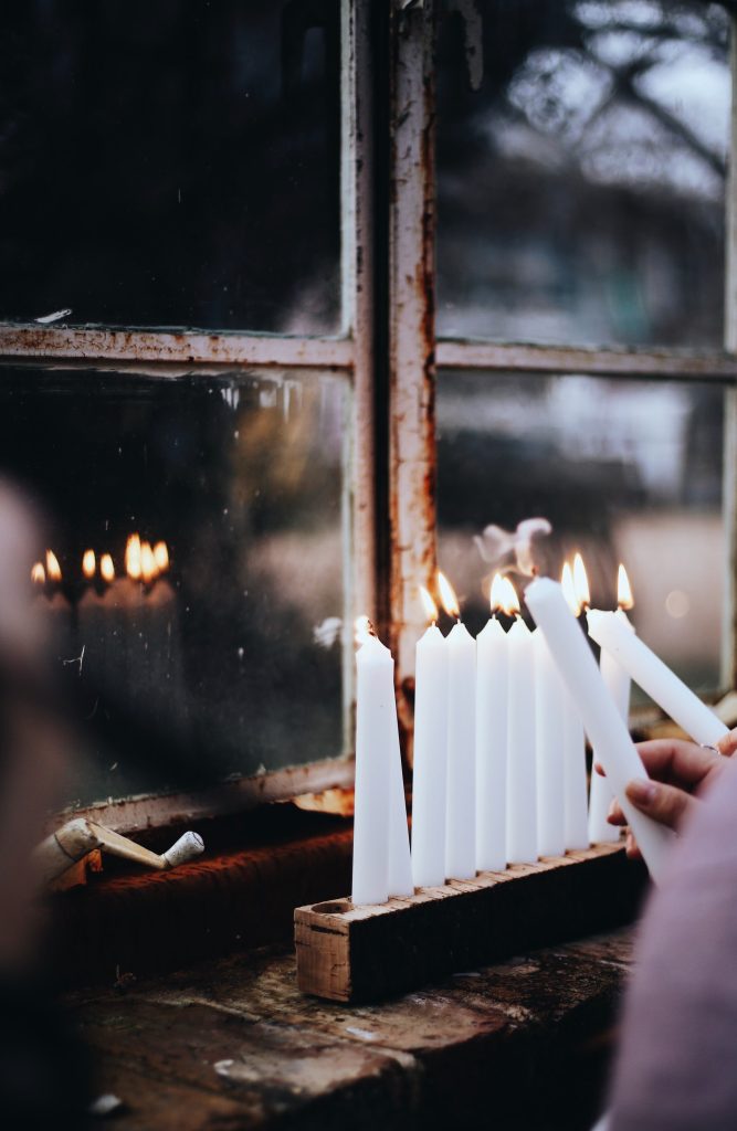 A person lighting white candles beside the window