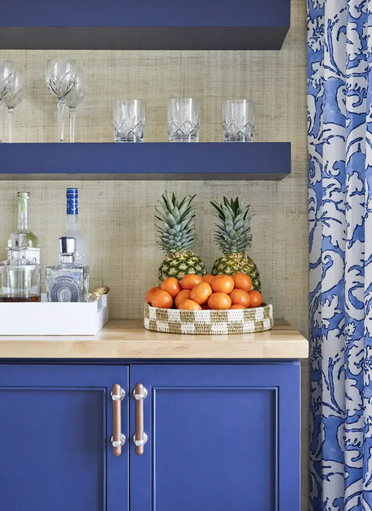 Kitchen details, oranges and pineapples in a bowl, bottles and glasses on a shelf